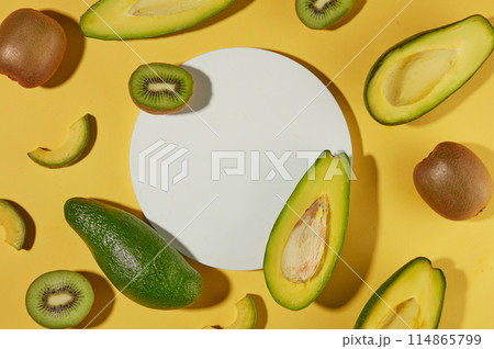 Several slices and halves of avocado and kiwi arranged over yellow background with a white podium. Minimal podium display for cosmetic product presentation Several slices and halves of avocado and kiwi arranged over yellow background with a white podium. Minimal podium display for cosmetic product presentation 114865799