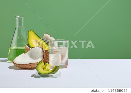 Layout for laboratory concept with some glassware and fresh fruits displayed. Halves of avocado and coconut featured on green background. Product can be showed in the blank space Layout for laboratory concept with some glassware and fresh fruits displayed. Halves of avocado and coconut featured on green background. Product can be showed in the blank space 114866035