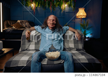 Man wearing zombie mask watching movie with popcorn 114867104