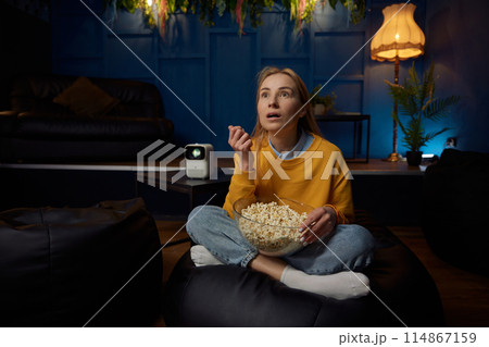 Young woman watching movie eating popcorn in living room Young woman watching movie eating popcorn in living room 114867159