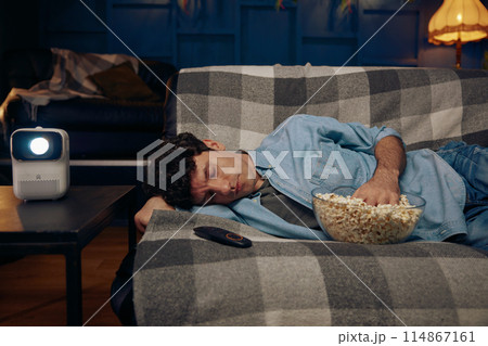 Young man with popcorn sleeping on sofa 114867161