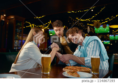 Cheerful friends having fun arm wrestling during rest in pub 114867193