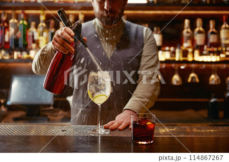 Bartender preparing cool cocktail standing in spray of flying liquid 114867267