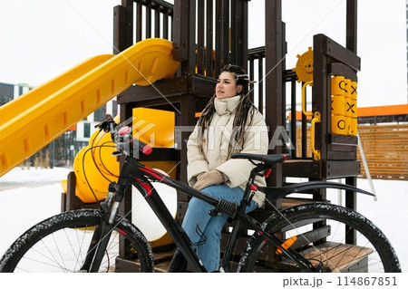 Woman Sitting on Bench Next to Bike 114867851