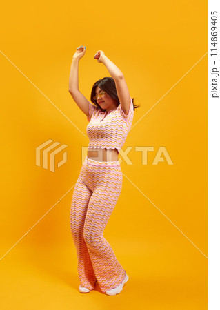 Party mood. Full length portrait of young Indian woman dancing of joy and happiness against vibrant yellow studio background. 114869405