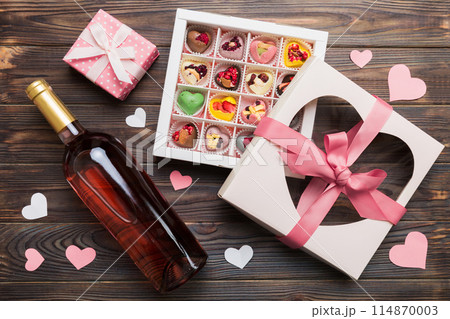 Bottle of red wine on colored background for Valentine Day with gift and chocolate. Heart shaped with gift box of chocolates top view with copy space Bottle of red wine on colored background for Valentine Day with gift and chocolate. Heart shaped with gift box of chocolates top view with copy space 114870003