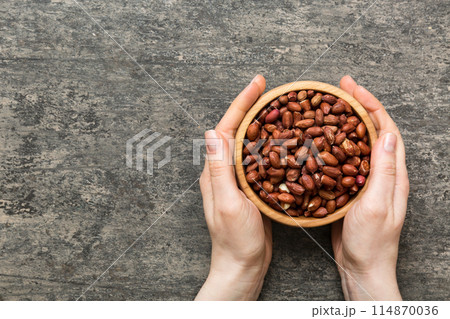 Woman hands holding a wooden bowl with peanuts. Healthy food and snack. Vegetarian snacks of different nuts Woman hands holding a wooden bowl with peanuts. Healthy food and snack. Vegetarian snacks of different nuts 114870036