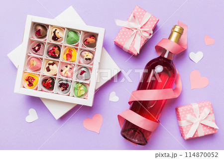 Bottle of red wine on colored background for Valentine Day with gift and chocolate. Heart shaped with gift box of chocolates top view with copy space Bottle of red wine on colored background for Valentine Day with gift and chocolate. Heart shaped with gift box of chocolates top view with copy space 114870052