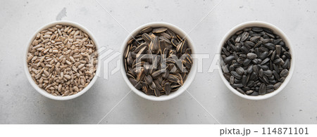 Whole and peeled with salted sunflower seeds in bowls on light background. 114871101