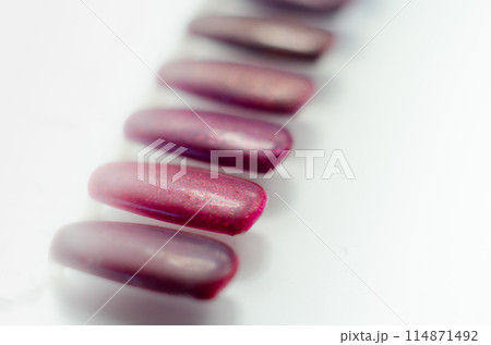 A row of purple patterns of painted nail plates are arranged on a white surface 114871492