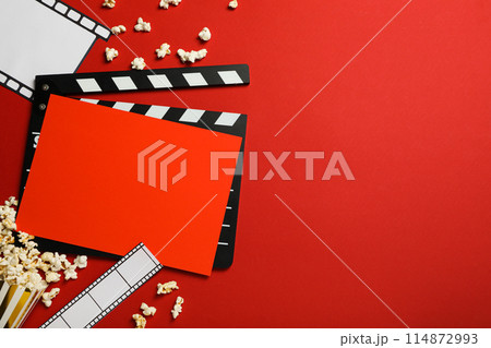 Clapperboard, paper cup with popcorn, film and reel on red background, space for text 114872993