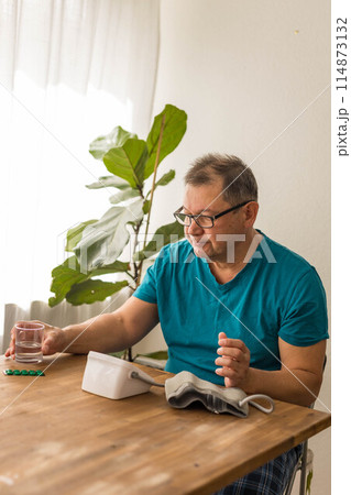Seniory man checks blood pressure with monitor on upper arm in room Seniory man checks blood pressure with monitor on upper arm in room 114873132