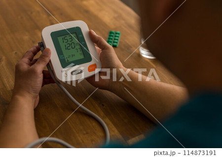 Seniory man checks blood pressure with monitor on upper arm in room  114873191