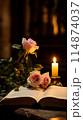 Two pink roses placed on an open bible beside a lit candle 114874037