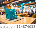 A laptop computer is placed on a wooden table inside a restaurant 114874038