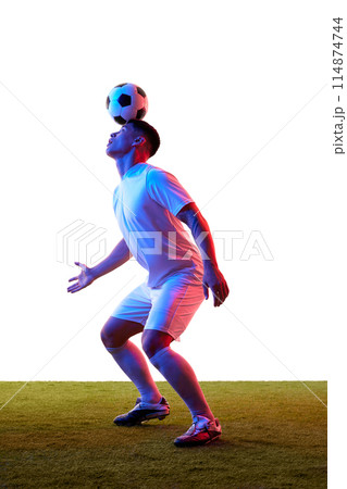 Soccer player balancing soccer ball on his head on green grassland in neon light against white studio background. 114874744