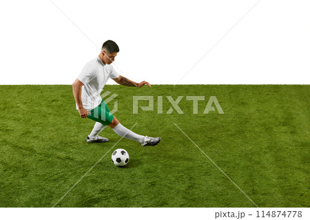 Young athletic man, soccer player in prepares to kicking ball on green grass field against white studio background. 114874778