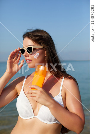 Beautiful woman applying cream sunscreen on tanned face. Sunscreen. Skin and body care. The girl uses a sunscreen for her skin. Portrait of a female holding suntan lotion and moisturizing sunscreen. 114876293