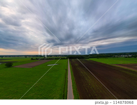 A road winds through fields under a dramatic sky, creating a picturesque scene of rural beauty 114878068