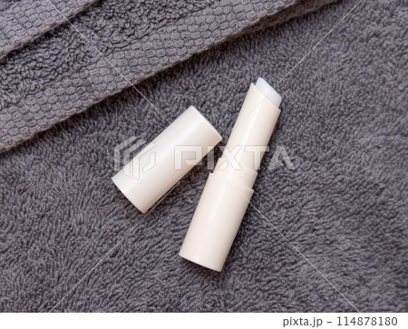 Opened lip balm stick on grey towels near basin and green monstera in bath, lid mockup 114878180