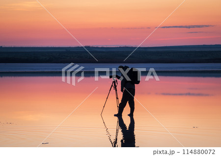 Photographer capturing sunset over tranquil waters Photographer capturing sunset over tranquil waters 114880072