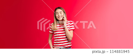 Carefree friendly good-looking blond asian girl having funny conversation, talking phone, close eyes joyfully smiling calling friend hold smartphone near ear, laughing over hilarious voice message 114881945