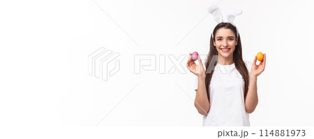 Portrait of lovely caucasian female in rabbit ears, showing two colored eggs and smiling, congratulate everyone with happy Easter day, celebrating and having fun, white background 114881973