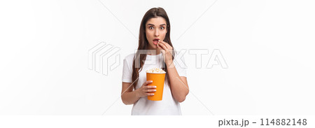 Entertainment, fun and holidays concept. Portrait of woman entertained, watching movie with interest, enjoying favorite tv series, eating popcorn and staring camera, stand white background Entertainment, fun and holidays concept. Portrait of woman entertained, watching movie with interest, enjoying favorite tv series, eating popcorn and staring camera, stand white background 114882148
