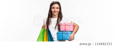 Shopping, holidays and lifestyle concept. Portrait of happy pretty young woman buying presents, holding wrapped boxed with gifts and show bags, smiling camera pleased, white background Shopping, holidays and lifestyle concept. Portrait of happy pretty young woman buying presents, holding wrapped boxed with gifts and show bags, smiling camera pleased, white background 114882151