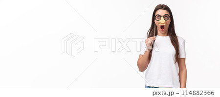 Entertainment, fun and holidays concept. Funny and cute young girl fool around, praying wearing glasses and nose mask, gasping amazed, look surprised standing white background 114882366