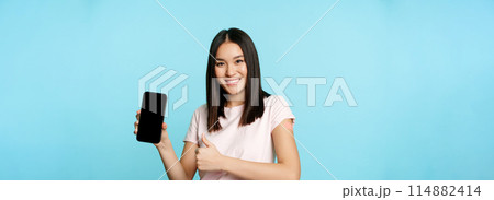 Smiling asian girl got vaccinate from coronavirus, showing thumbs up and smartphone app interface, concept of health passport, international vaccination certificate from covid 114882414