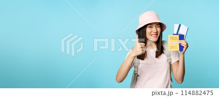 Enthusiastic girl traveller, asian tourist shows thumbs up and international vaccine certificate, health passport and flight tickets, standing over blue background Enthusiastic girl traveller, asian tourist shows thumbs up and international vaccine certificate, health passport and flight tickets, standing over blue background 114882475