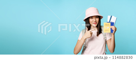 Smiling korean tourist shows her passport, vaccination certificate from coronavirus disease, getting vaccine shot to travel, standing over blue background 114882830