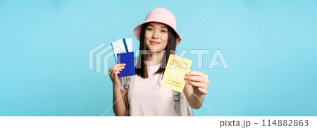 Happy smiling asian tourist, girl shows international vaccination passport, health passport and flight tickets, getting abroad after covid-19 vaccine shot, blue background Happy smiling asian tourist, girl shows international vaccination passport, health passport and flight tickets, getting abroad after covid-19 vaccine shot, blue background 114882863