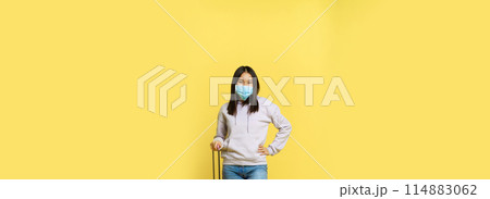 Full length shot smiling korean female tourist in medical face mask, posing with suitcase, going on vacation, standing over yellow background Full length shot smiling korean female tourist in medical face mask, posing with suitcase, going on vacation, standing over yellow background 114883062