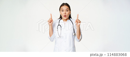 Portrait of surprised female asian doctor, physician pointing fingers up, showing amazing news, big promo, white background Portrait of surprised female asian doctor, physician pointing fingers up, showing amazing news, big promo, white background 114883068