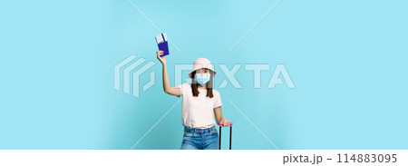 Full length of happy asian tourist, girl travelling abroad, posing with her suitcase in medical face mask, showing passport and tickets, blue background Full length of happy asian tourist, girl travelling abroad, posing with her suitcase in medical face mask, showing passport and tickets, blue background 114883095
