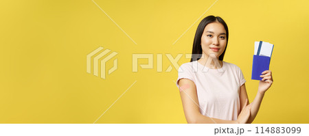 Smiling vaccinated from covid asian girl, showing passport with tickets, getting coronavirus vaccine shot for travelling abroad, yellow background Smiling vaccinated from covid asian girl, showing passport with tickets, getting coronavirus vaccine shot for travelling abroad, yellow background 114883099