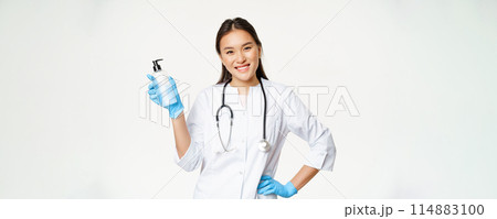 Smiling asian physician holding hand sanitizer in rubber gloves, showing bottle with antiseptic for coronavirus prevention, white background Smiling asian physician holding hand sanitizer in rubber gloves, showing bottle with antiseptic for coronavirus prevention, white background 114883100