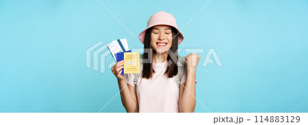 Happy asian girl triumphing, showing vaccination certificate, health passport and flight tickets, celebrating about trip, tourist feeling joy, standing over blue background Happy asian girl triumphing, showing vaccination certificate, health passport and flight tickets, celebrating about trip, tourist feeling joy, standing over blue background 114883129