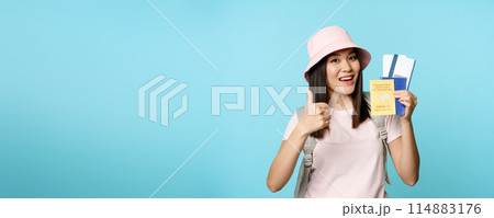 Smiling happy asian tourist, girl shows thumbs up and international vaccination certificate, vaccine passport and tickets, standing over blue background 114883176