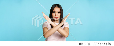 Stop. Concerned asian woman showing cross sign, saying no, raise awareness, standing over blue background 114883310