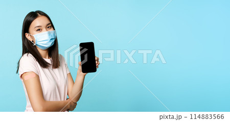Asian woman in medical face mask, showing arm with patch after covid-19 vaccine, smartphone screen with app interface, concept of vaccination certificate, health passport Asian woman in medical face mask, showing arm with patch after covid-19 vaccine, smartphone screen with app interface, concept of vaccination certificate, health passport 114883566