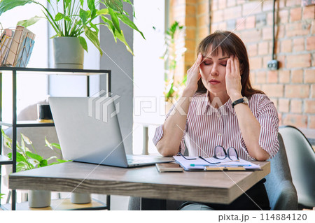 Mature tired worried tense woman at workplace experiencing stress headache Mature tired worried tense woman at workplace experiencing stress headache 114884120