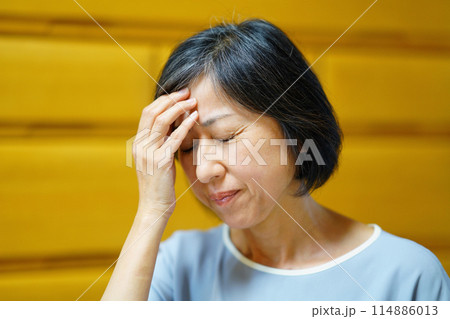 額に手を当てて不調を訴える中年女性 114886013