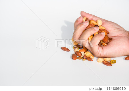 A hand is holding a handful of nuts, including almonds, cashews, and peanuts A hand is holding a handful of nuts, including almonds, cashews, and peanuts 114886910