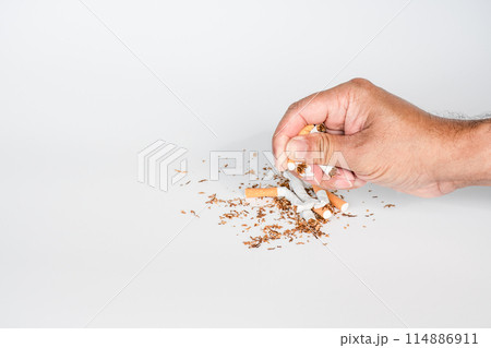 A hand is crushing cigarette butts on a white surface A hand is crushing cigarette butts on a white surface 114886911