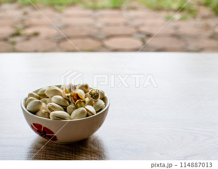 A bowl of pistachios sits on a wooden table 114887013