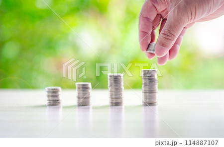 A hand is reaching for a stack of coins, which are piled up in a pyramid shape A hand is reaching for a stack of coins, which are piled up in a pyramid shape 114887107