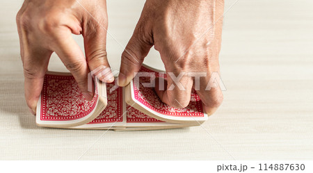 A hand is bending a red playing card A hand is bending a red playing card 114887630